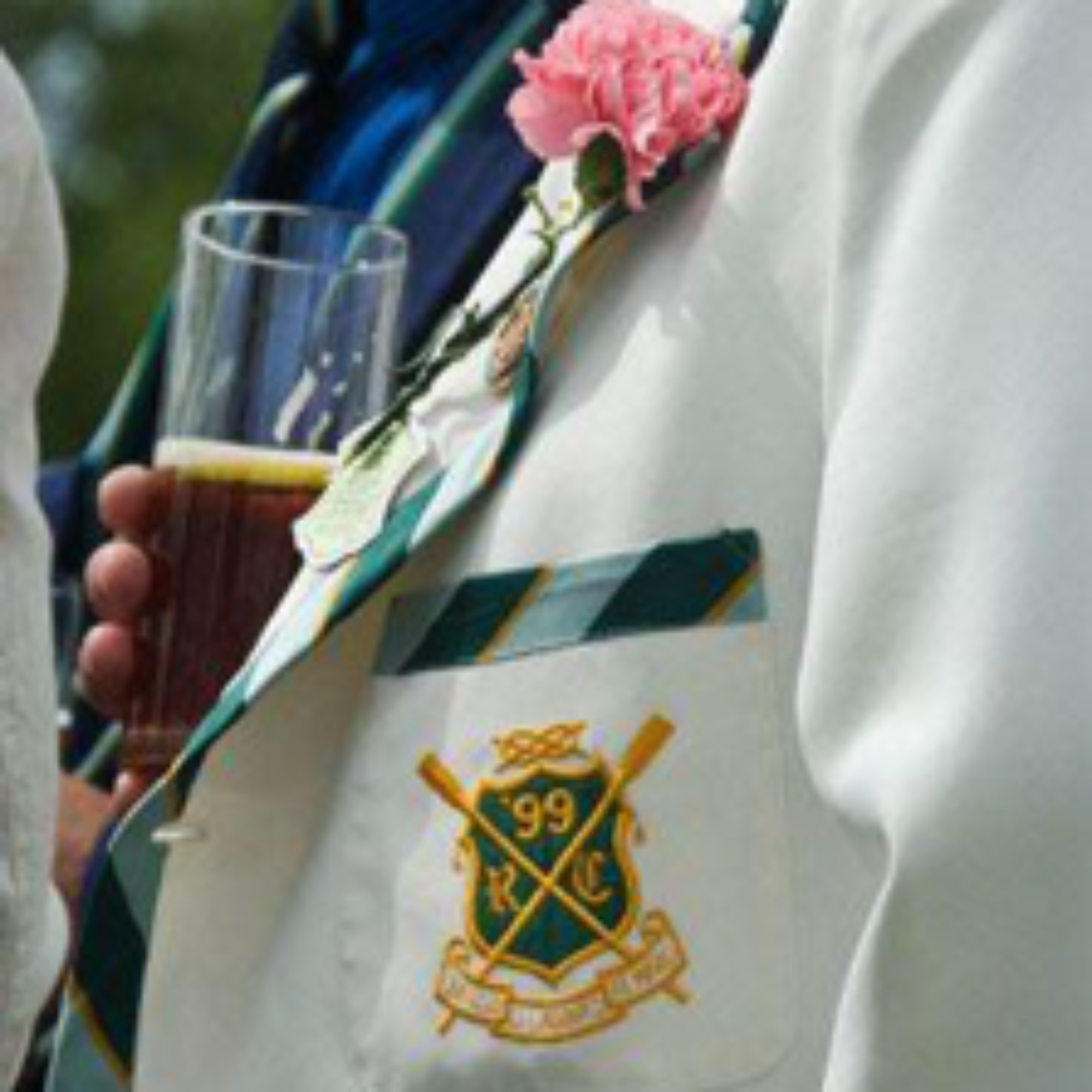 Man wearing a white blazer with green detailing at Henley Royal Regatta. He is holding a pint of beer.