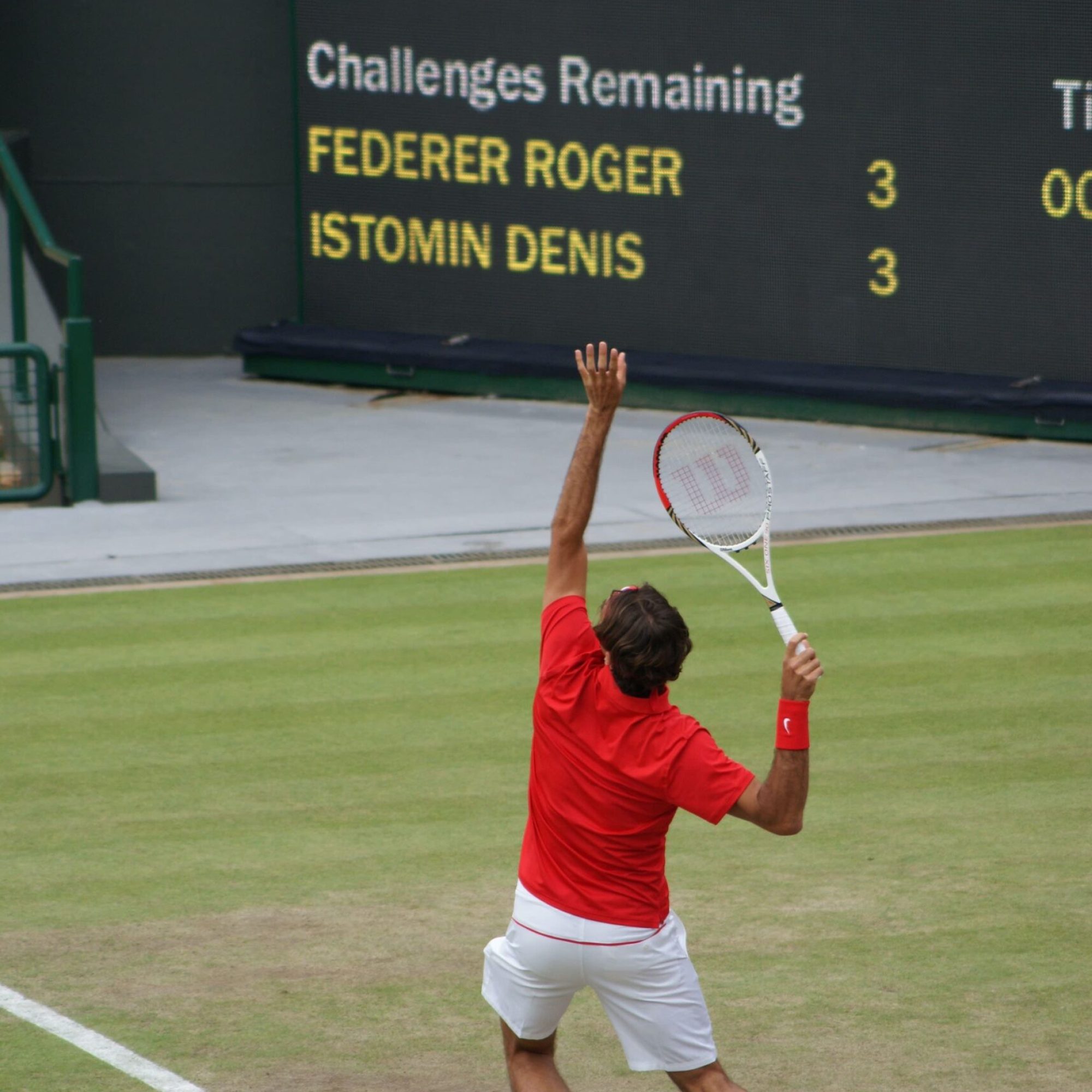 photo of a tennis player at Wimbledon in a red top and white shorts about to serve
